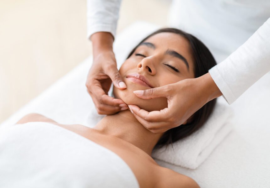 Beautiful Young Indian Woman Getting Face Lifting Massage In Luxury Spa Salon, Masseur Making Double Chin Treatment Procedure To Relaxed Lady Lying With Eyes Closed, Closeup Portrait